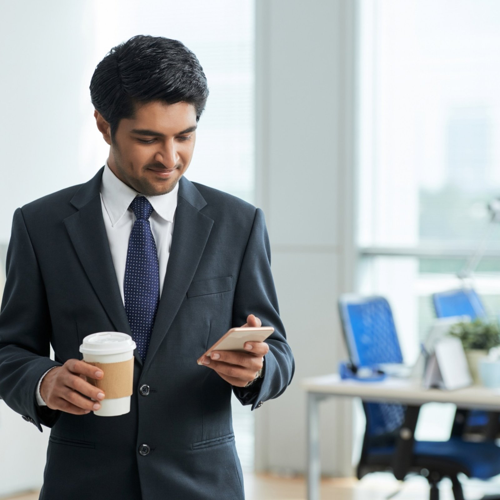 man-suit-standing-office-holding-takeaway-coffee-using-smartphone